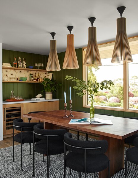In the dining room, enlarging the window opening brings more light and connections to the exterior, while a new wet bar creates opportunities for entertaining. The table is custom, and chairs and rug are from CB2. The pendant lights are Design Within Reach.