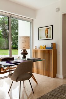 In the office, a Reale table by Carlo Mollino and a Conference chair by Eero Saarinen for Knoll look out on the gardens. The lamp is from Le Bon Marché. On the wall is a photograph by Dutch artist Barry Marré, and below it is a custom oak heater cover designed by Pilon.