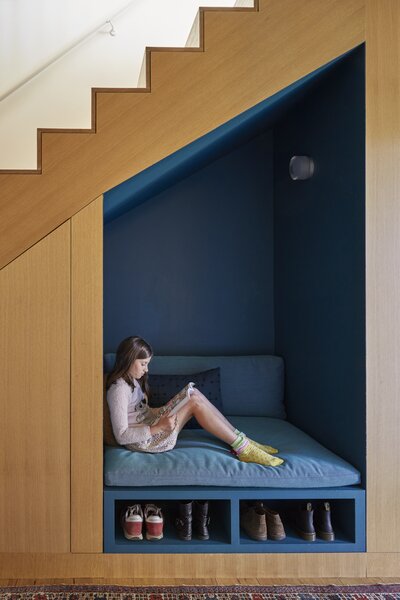 The couple's daughter reads in the cozy nook just inside the front door painted in a vibrant blue from Benjamin Moore. Of the storage area below, Fredrik says, "In Sweden, there's always a place to sit and take off your shoes. This is a version of that."
