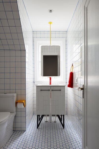 The new upstairs bathroom, inspired by a 1992 Robin Williams movie, juxtaposes hexagonal and rectangular white tiles, as well as blue grout with four pops of yellow metal (matching the color of the original house's front door).