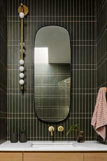 The guest room's bathroom features a sconce by Lindsey Adelman and all-green tiles. Since this bathroom is also the powder room, the owners wanted it to be fun.
