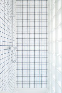 The square tiles of the shower walls mimic the squares of the glass-block wall that delineates the bathroom.