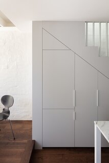 White-painted storage cabinets are built-in to the wall beneath the staircase.